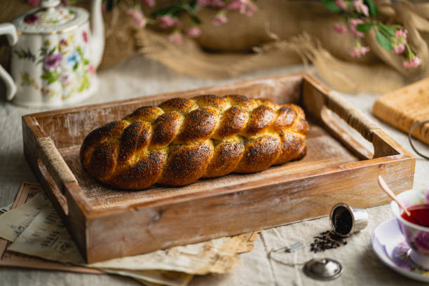 nahaufnahme eines laibs eines challah-brotes mit mohn auf einem holztablett mit vintage-papieren - hanukkah loaf of bread food bread stock-fotos und bilder