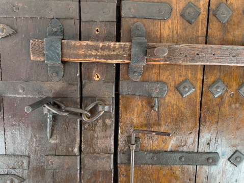 Old wood doors with iron hardware, chain and spike closure. Wood plank slides across both doors, held by iron brackets to lock the doors and hold off an intruder. Medieval fortress doors