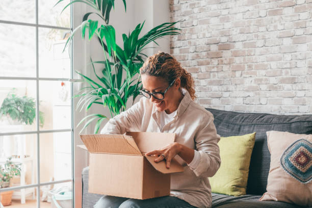 Overjoyed woman seated on sofa hold on lap small cardboard box open parcel client feels satisfied bought goods in internet, happy addressee received package from friend, quick delivery service concept mujer encantada sentada en el sofá sostener en el regazo pequeña caja de cartón abrir paquete cliente se siente satisfecho comprando productos en internet, feliz destinatario recibió paquete de amigo, concepto de servicio de entrega rápida