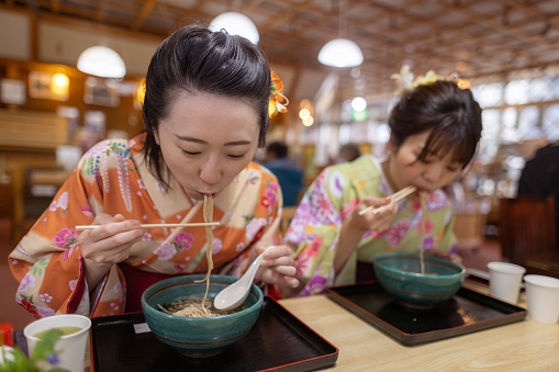 Female friends in kimono eating soba in Japanese restaurant