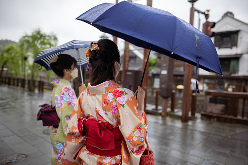 Rear view of Japanese female friends in kimono visiting traditional Japanese village in a rainy day