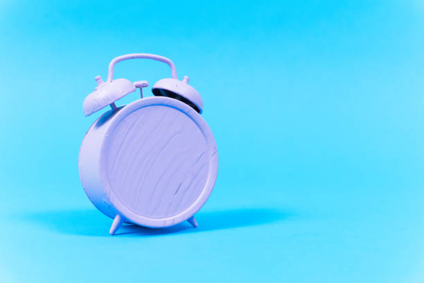 istock Vintage alarm clock with a handle and bells is completely painted over with purple paint, front view, blue background, copy space. Art object is a metaphor for routine fuss 1396570725