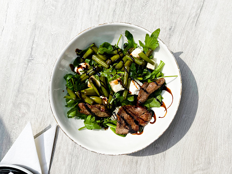 Top view of beef roasted meat with balsamic vinegar, green beans, and arugula on a white plate. BBQ. Balsamic. Cooking. Selective. Vinegar. Nutrition. Restaurant. Barbecued. Meaty. Cook. Cut. Fresh