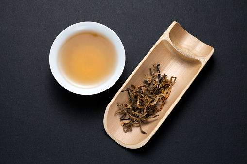 A cup of Yunnan black tea with dry tea leaves on black background. Top view.