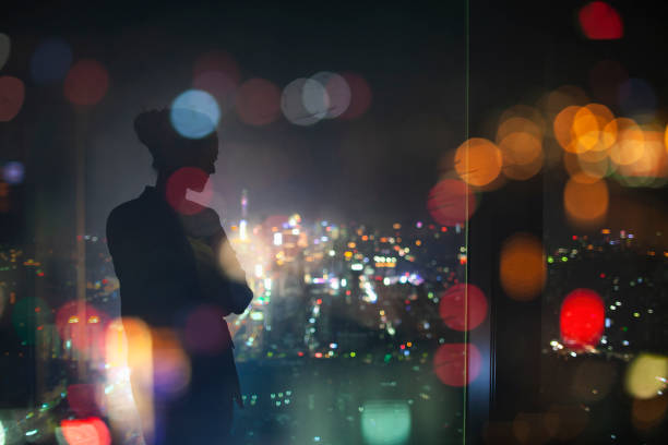 silhouette di giovane donna adulta in piedi in contemplazione di notte nella finestra di vetro della città urbana riflesso, effetto multistrato, immagine composita - reflection women contemplation ethnic foto e immagini stock