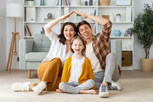 Mother, father and child girl in the room with a symbol of roof. Concept of housing for young family.