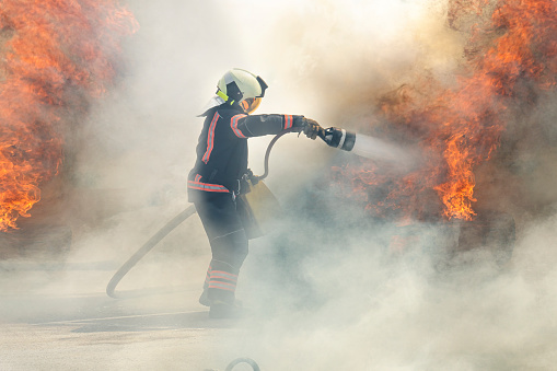 firefighter extinguishes a fire. The hero firefighter stands among the smoke and fire and extinguishes the fire with a stream of water.