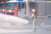strong flow of water and foam from the fire hose in the firefighter's hand. Firefighters extinguish a fire from a fire truck. extinguishing fire with foam