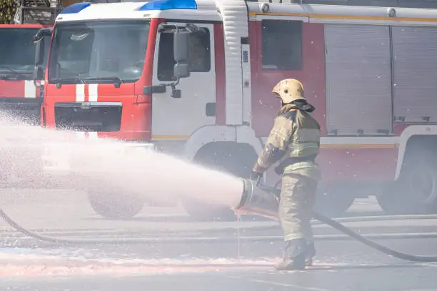 Photo of strong flow of water and foam from the fire hose in the firefighter's hand. Firefighters extinguish a fire from a fire truck. extinguishing fire with foam