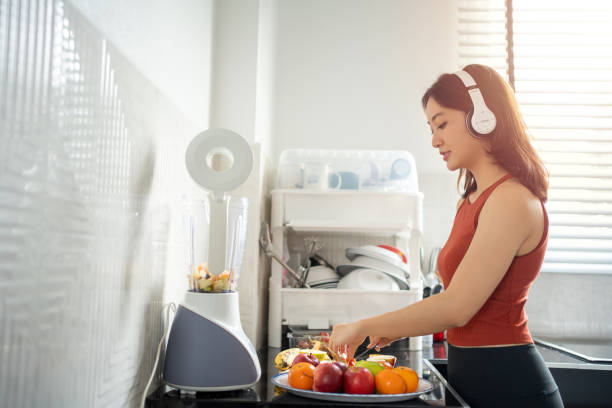 The sportswoman making smoothies from fruits in the kitchen at home while listening to music through headphones - lifestyles concepts stock photo