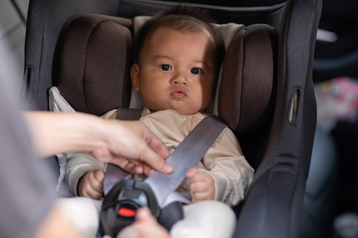 Mother put cute baby to car seat and secure with safety belts. Asian infant baby sit in baby seat and looking around in car.mom buckling her son to car seat.Baby safety on car concept