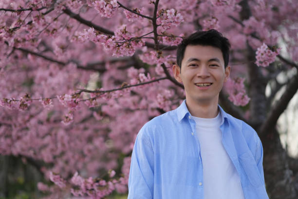 istock smiling handsome Asian young man, pink sakura flower tree 1396600881