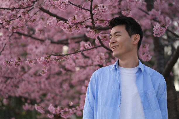 istock smiling handsome Asian young man side face, with pink cherry blossom tree 1396600888