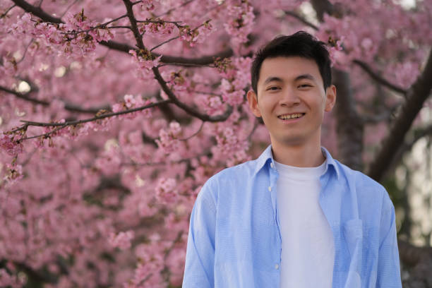 istock happy handsome Asian young man, with beautiful pink sakura flower tree 1396600898