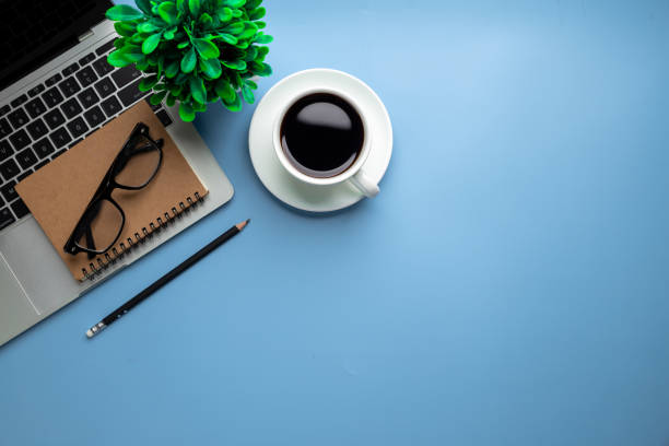 istock Flat lay, top view office table desk. Workspace with, laptop,office supplies, pencil, green leaf, and coffee cup on blue background. 1396605385