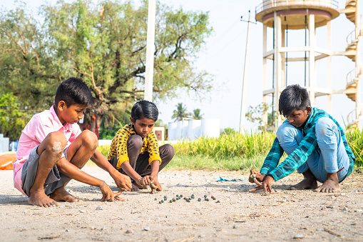 Indian village kids playing goli or marbles on near paddy field - concept of traditional game, summer holidays and leisure activities
