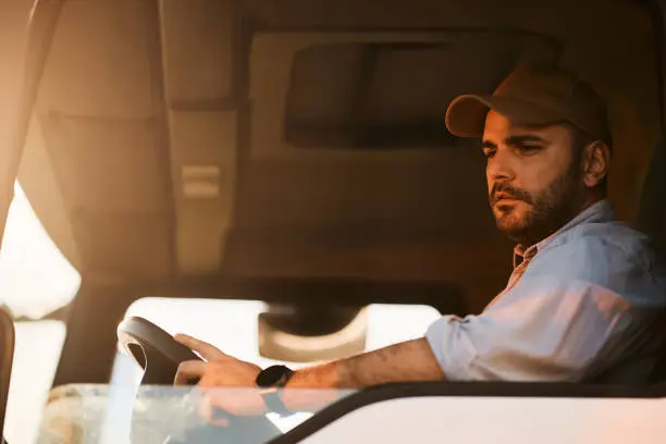 Photo of Young truck driver looking at side view mirror while driving in reverse.