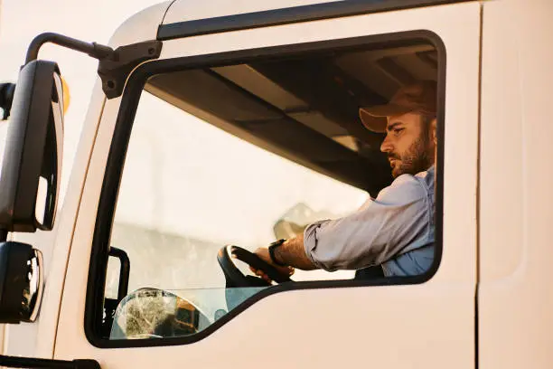 Photo of Professional truck driver driving in reverse while looking in side view mirror.