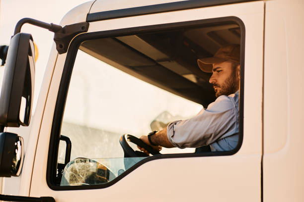 профессиональный водитель грузовика едет задним ходом, глядя в зеркало бокового вида. - side view mirror стоковые фото и изображения