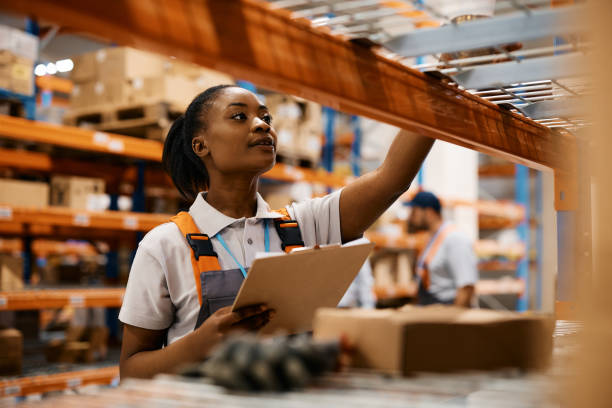 istock Black female worker checking inventory on shelves of distribution warehouse. 1396606540