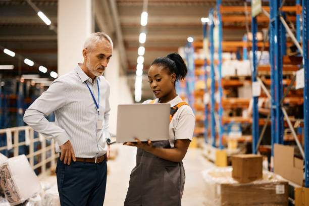 istock Black female worker and mature foreman using laptop while working at distribution warehouse. 1396606658