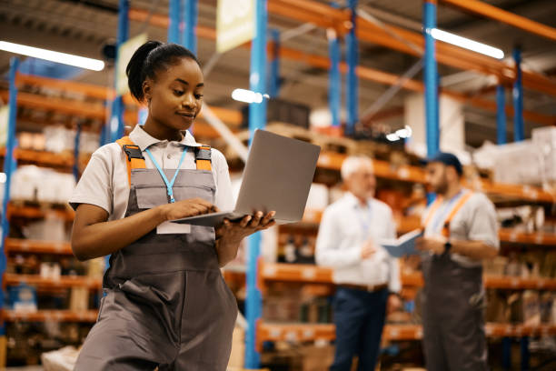 istock Young black woman using laptop while working at distribution warehouse. 1396606660