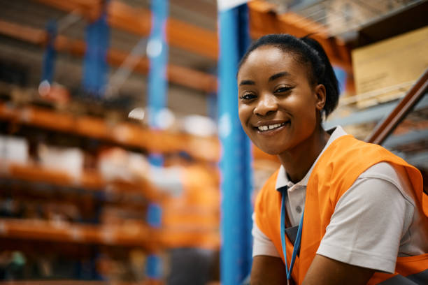 glückliche schwarze arbeiterin im auslieferungslager schaut in die kamera. - warehouse worker stock-fotos und bilder