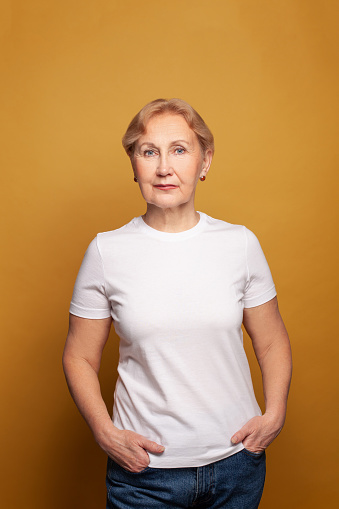 Mature woman in white t-shirt on bright yellow studio wall background