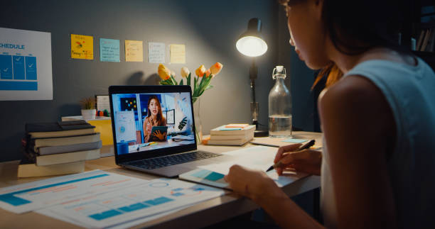 Asia businesswoman using laptop talk to colleagues about plan in video call meeting at living room at home. stock photo