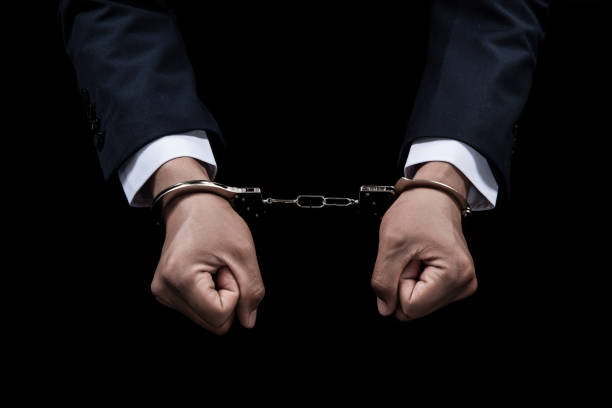 istock Handcuffed hands of a prisoner on black background. 1396612386