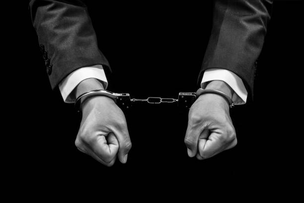 istock Handcuffed hands of a prisoner on black background.Black and white 1396612390