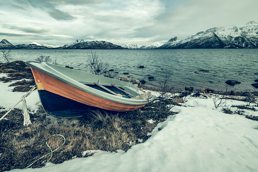 Boat on the shore of the Møklandsfjord on the Vesteralen island in Norway during winter. Wide panoramic image with snow covered mountains surrounding the fjord.