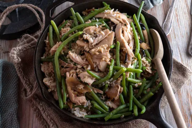 Delicious and healthy fitness meal. Cooked with chicken breast, brown rice, green beans and onions. Served in a rustic cast iron frying pan on wooden table background. Ready to eat