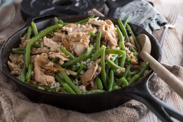 Healthy fitness meal for strenght training or body building with shredded chicken, brown rice and green beans. Served in a frying pan on rustic table background. Ready to eat.  Prep meal