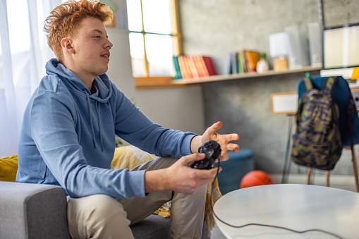 Caucasian redhead teenage boy playing video games, feeling frustrated after he lost the game