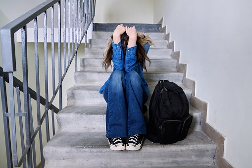 Sad frustrated young woman sitting on the steps. Teenage depressed female student with backpack, emotion problems trouble concept