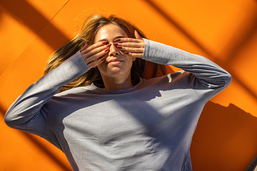 High anlge view og young Caucasian woman lying on the orange background and covering her eyes