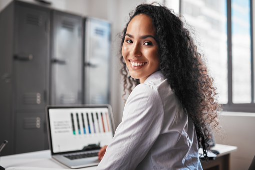 Portrait of young mixed race business woman using a laptop to monitor her startup as a freelancer in an office. Happy hispanic entrepreneur using a computer to analyse progress charts on her business