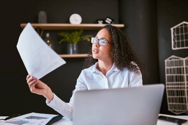 istock Young mixed race business woman thinking and reading paperwork while using a laptop in an office. Ambitious hispanic entrepreneur using documents and a computer to plan for her startup as a freelancer 1396617281