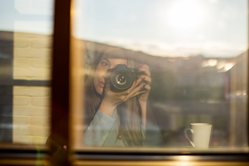 Reflection in the window of young woman with camera