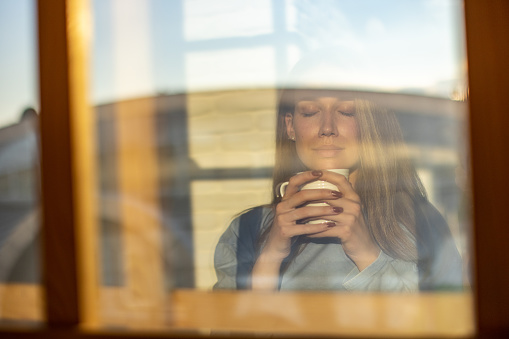Reflection in the window of young Caucasian woman drinking coffee