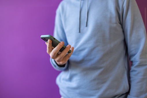 Unrecognizable Caucasian redhead teenage boy using mobile phone. Purple background