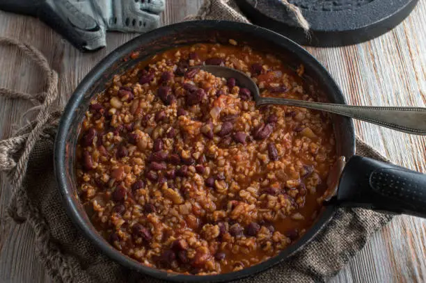 Healthy fitness meal with brown rice, kidney beans, vegetables in a delicious tomato sauce. Served in a frying pan on rustic and wooden table background. Vegetarian and vegan dish.