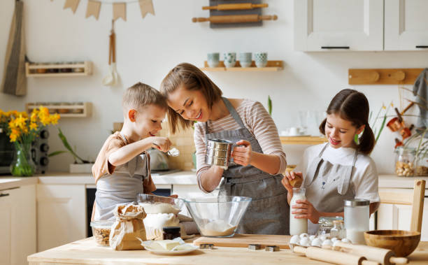 happy woman and cute children cooking together in kitchen - family mother domestic life food imagens e fotografias de stock