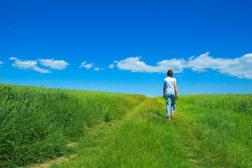 person walking through bright green field under blue sky with clouds