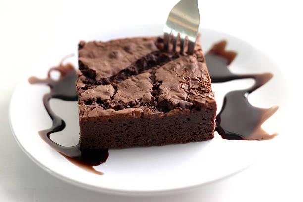 Brownie with chocolate fudge Brownie with chocolate fudge on the sides in a white dish and a fork on it appitite stock pictures, royalty-free photos & images