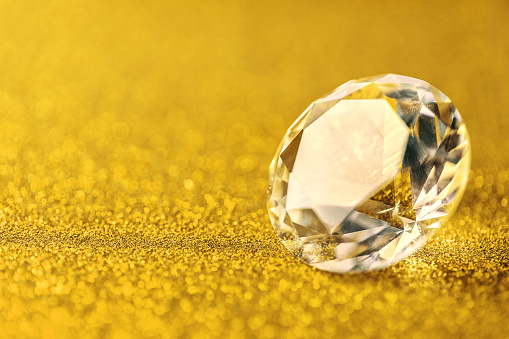 Grand royal pure diamond on golden sparkling sequins background, macro. Big brilliant closeup. Gem on yellow backdrop