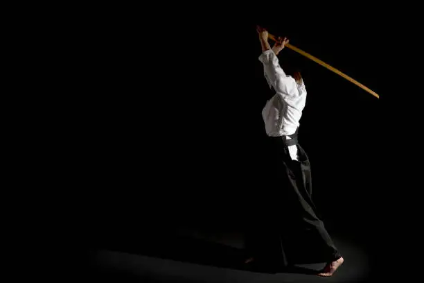 A girl in black hakama standing in fighting pose with wooden sword bokken over black background. Shallow depth of field.