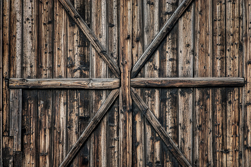 Detail of old wooden barn door with weathered planks, cross, knots and rings.