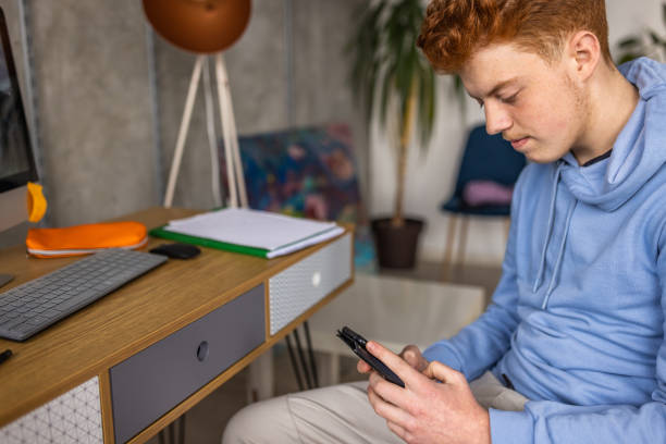 caucasian redhead teenage boy using mobile phone - homework teenager mobile phone school imagens e fotografias de stock